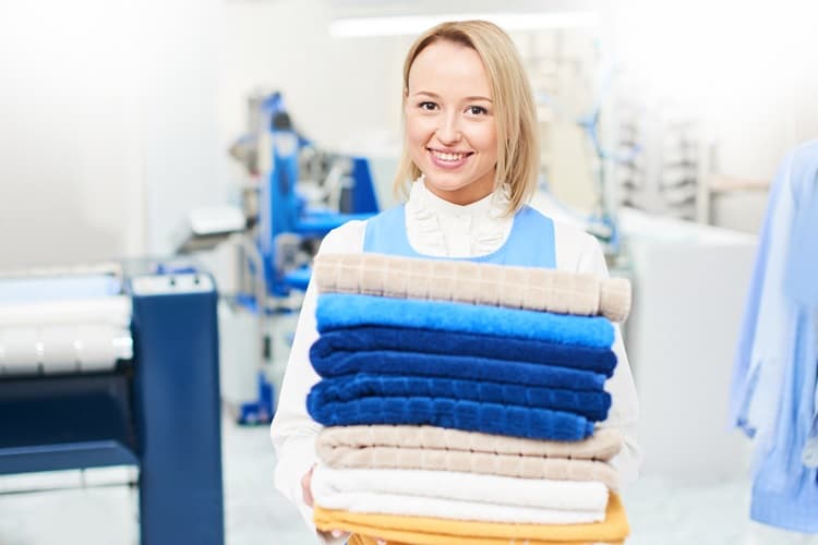A smiling lady holding folding clothes in a laundry shop